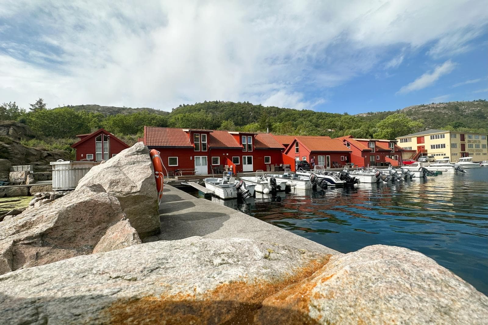 Rote Holzhäuser und Boote am Steg in Ramsland bei Spangereid an einem Sommertag